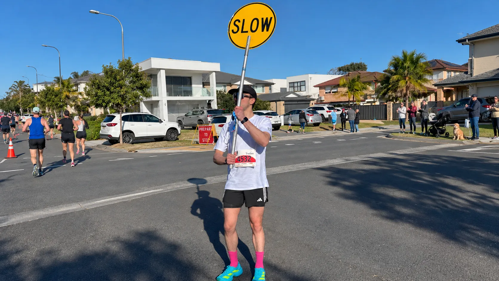 A runner holding a yellow slow sign beside a road race as participants pass