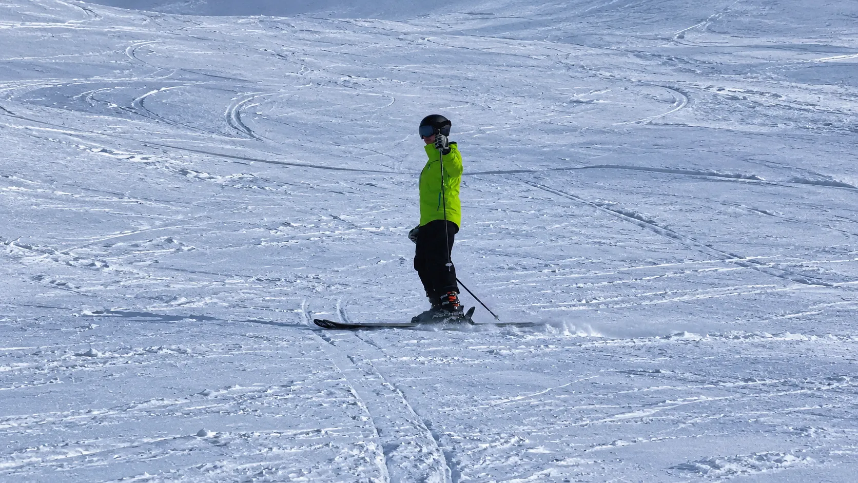 A skier in a green jacket on a wide snowy slope