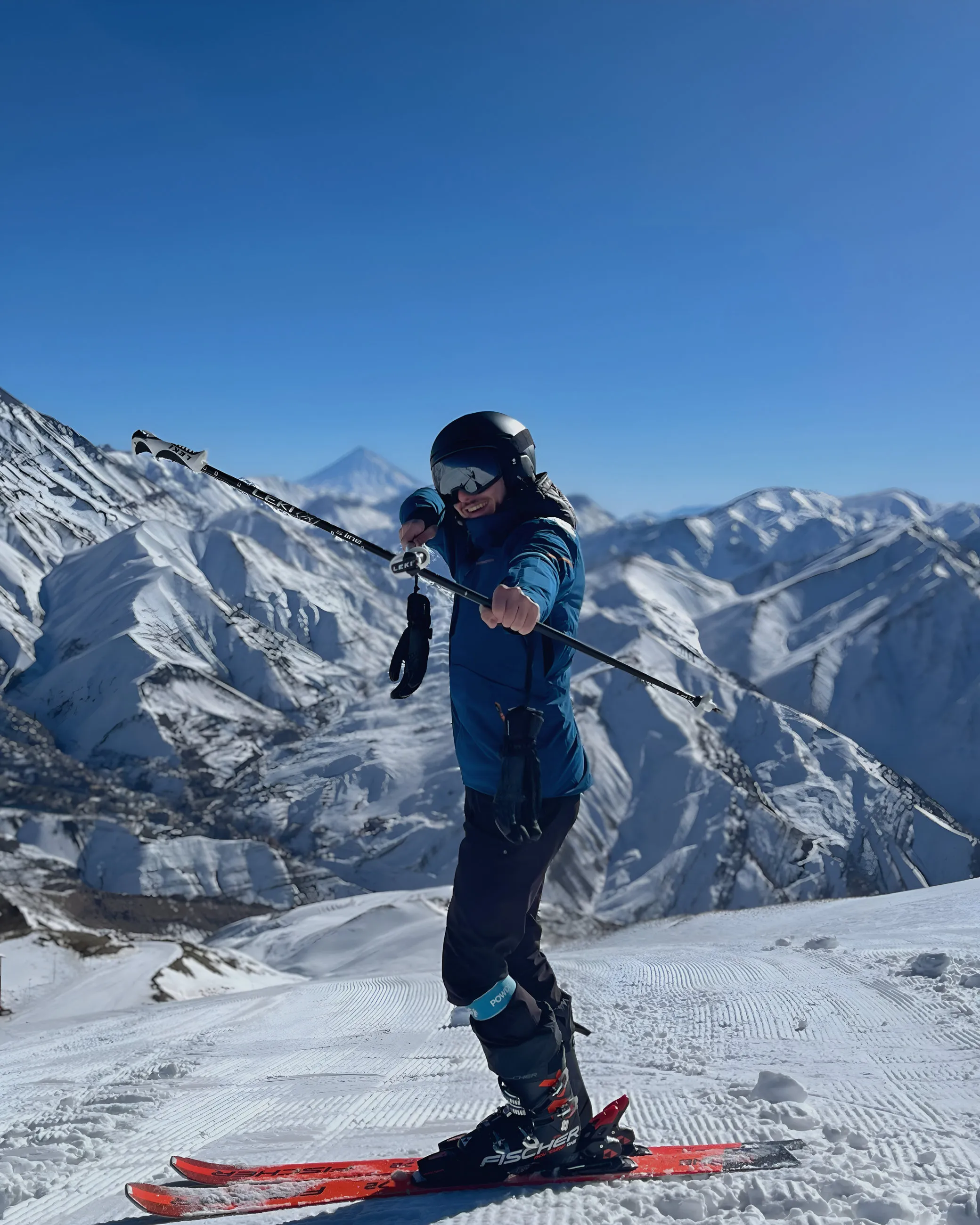 Me standing on skis on a mountain slope, holding ski poles, with snowy ridges behind