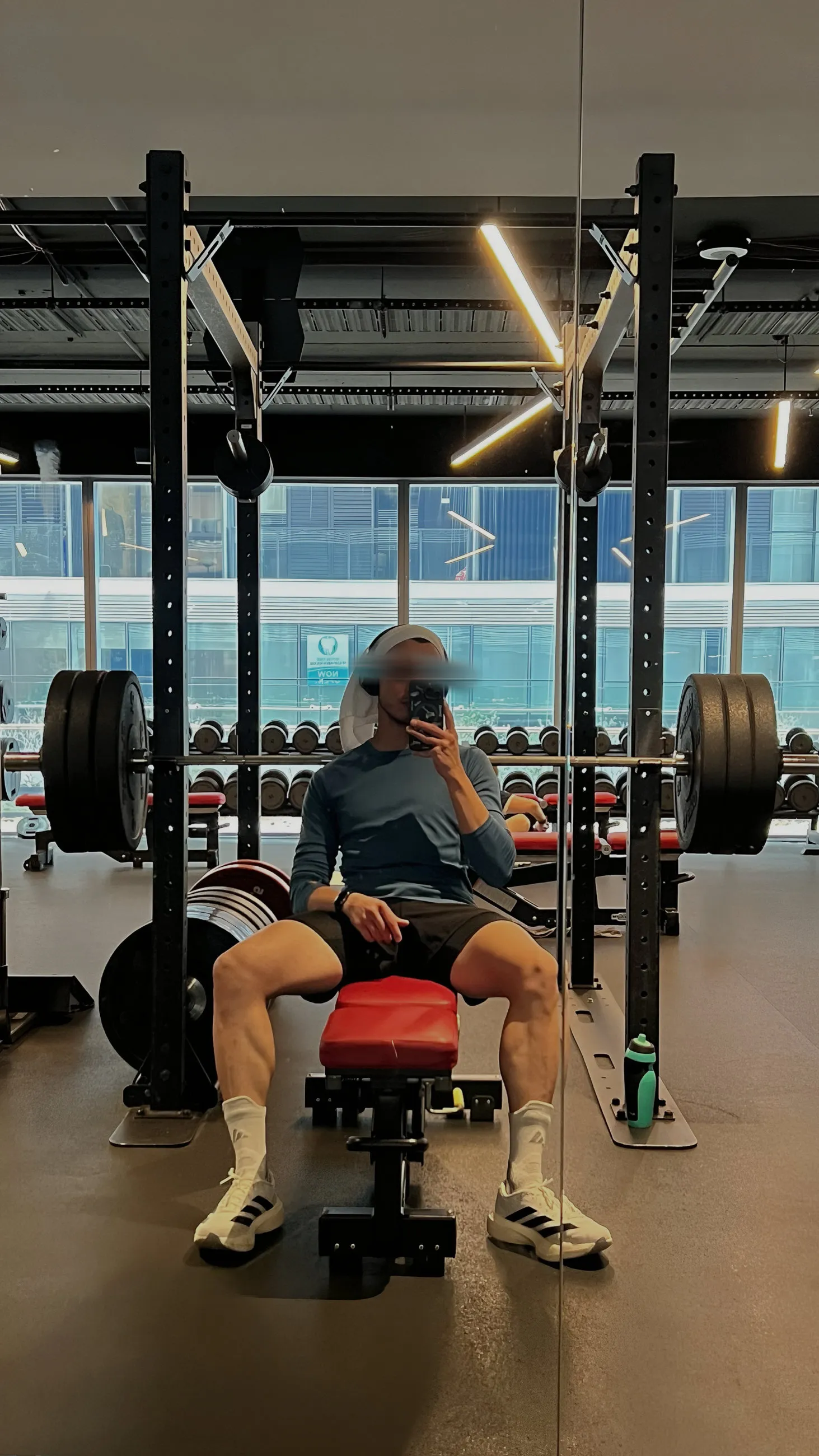 Me seated at a bench in a gym, with a loaded bar and weight rack behind